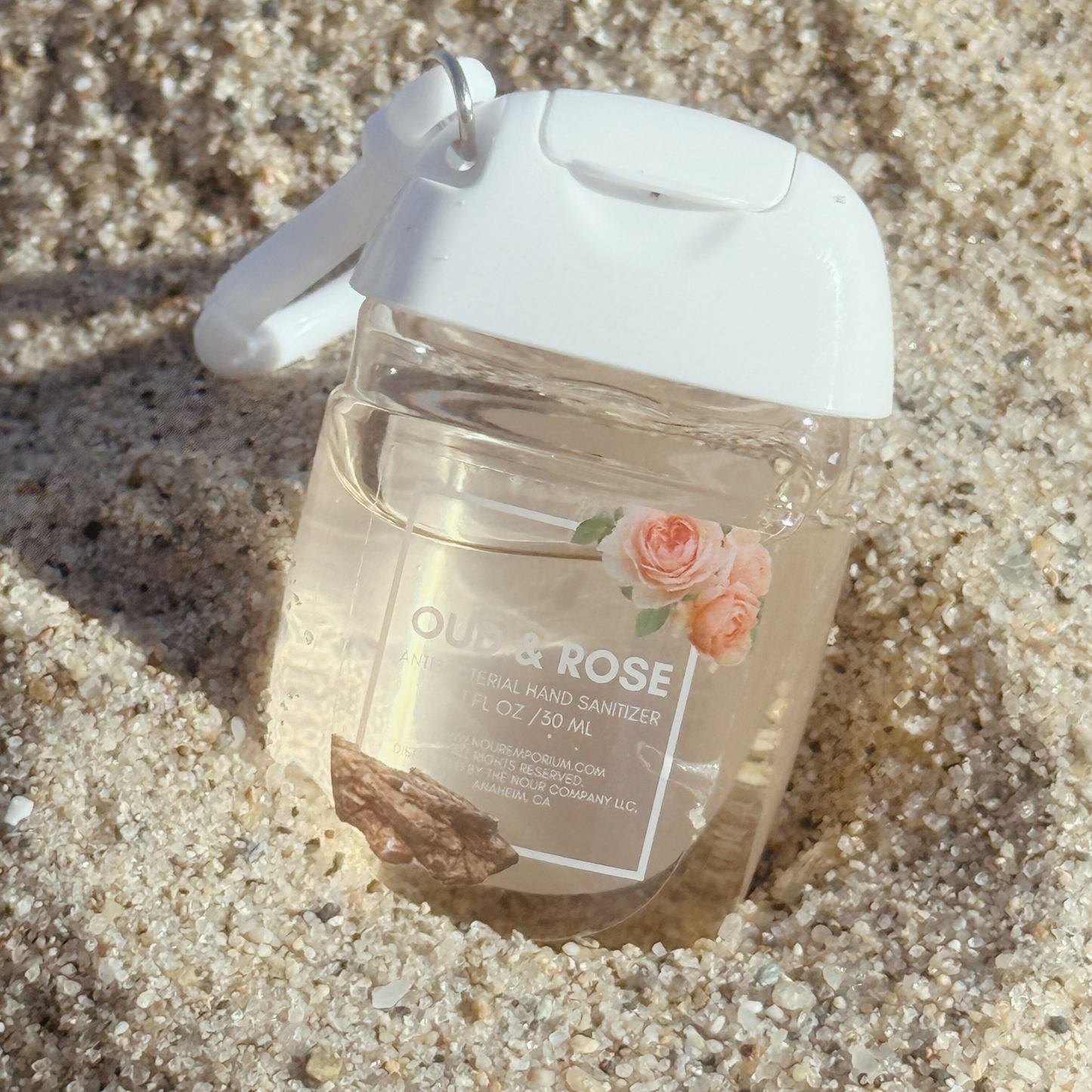 Hand sanitizer bottle labeled 'Oud & Rose' on sand